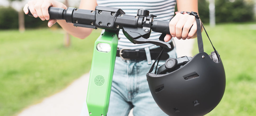 Persona circulando en patinete eléctrico con el casco de la mano
