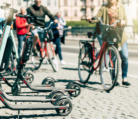 Patinetes eléctricos aparcados en la acera mientras personas pasan en bicicleta