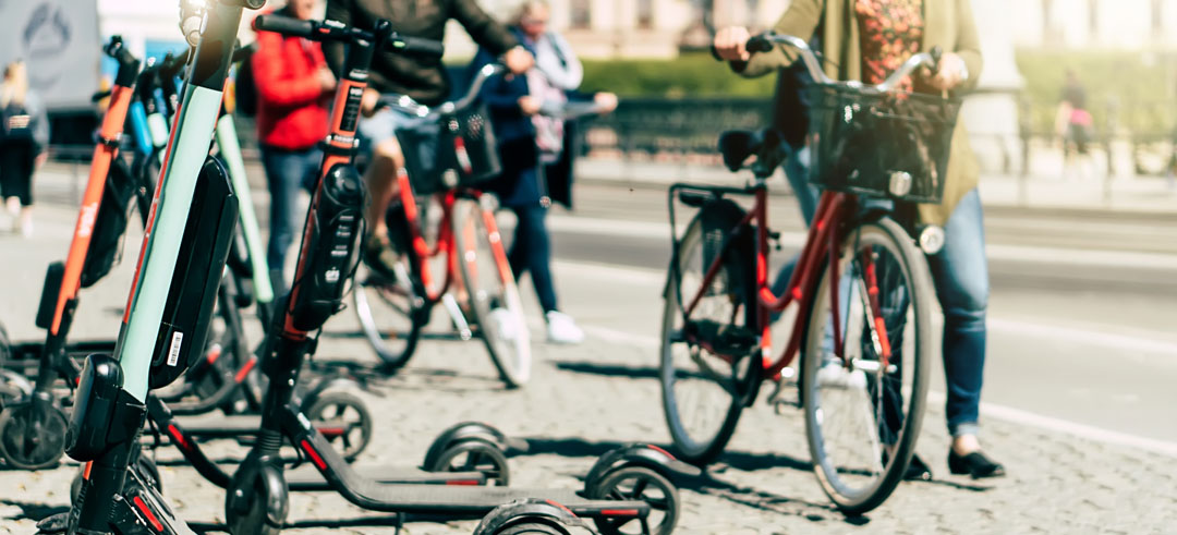 Patinetes eléctricos aparcados en la acera mientras personas pasan en bicicleta